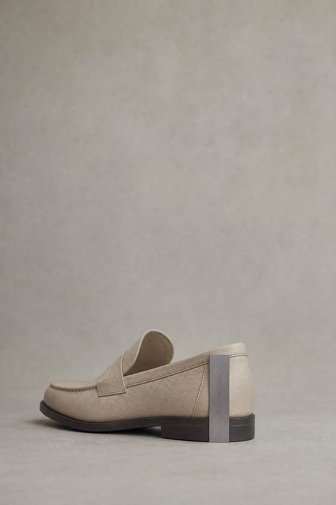 A gauge blade held upright against the back of a plain loafer, reaching from the floor to the lowest point of the shoe opening.