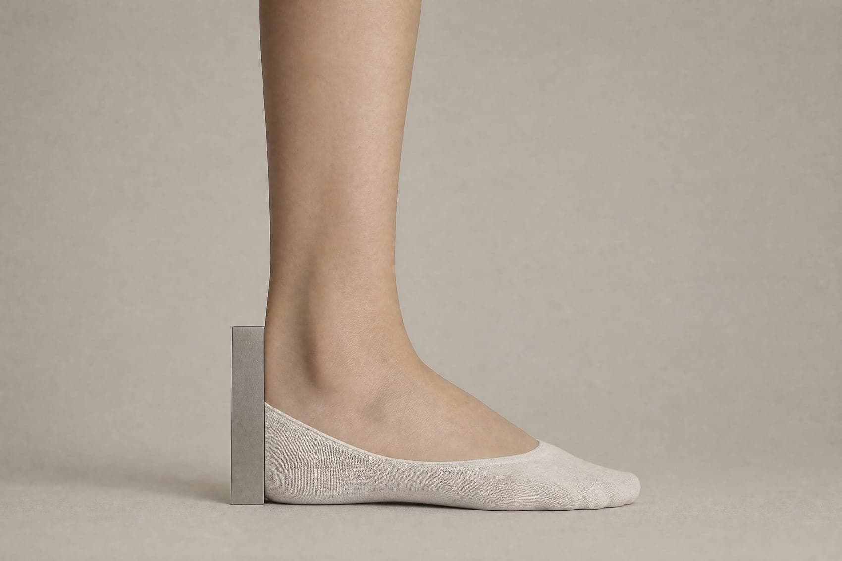 A gauge blade held against a bare heel wearing a low-cut sock, reaching from the floor to the top edge of the sock.
